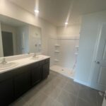 White bathroom with double vanity and shower.