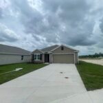 Tan house with driveway and green grass.