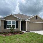 Tan house with a garage and lawn.