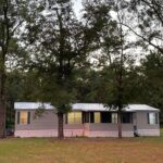 Gray mobile home surrounded by trees.