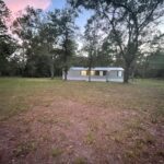 A white mobile home in a grassy yard.