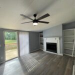 Living room with fireplace, ceiling fan, and deck view.