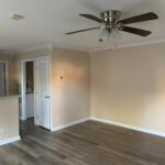 Empty living room with ceiling fan and wood floors.