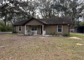 Brown house with white porch, trees.